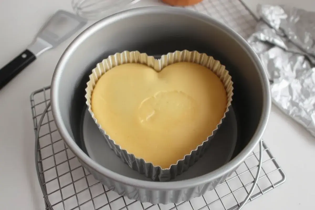 A freshly baked heart-shaped cake made with a DIY aluminum foil mold, sitting on a cooling rack